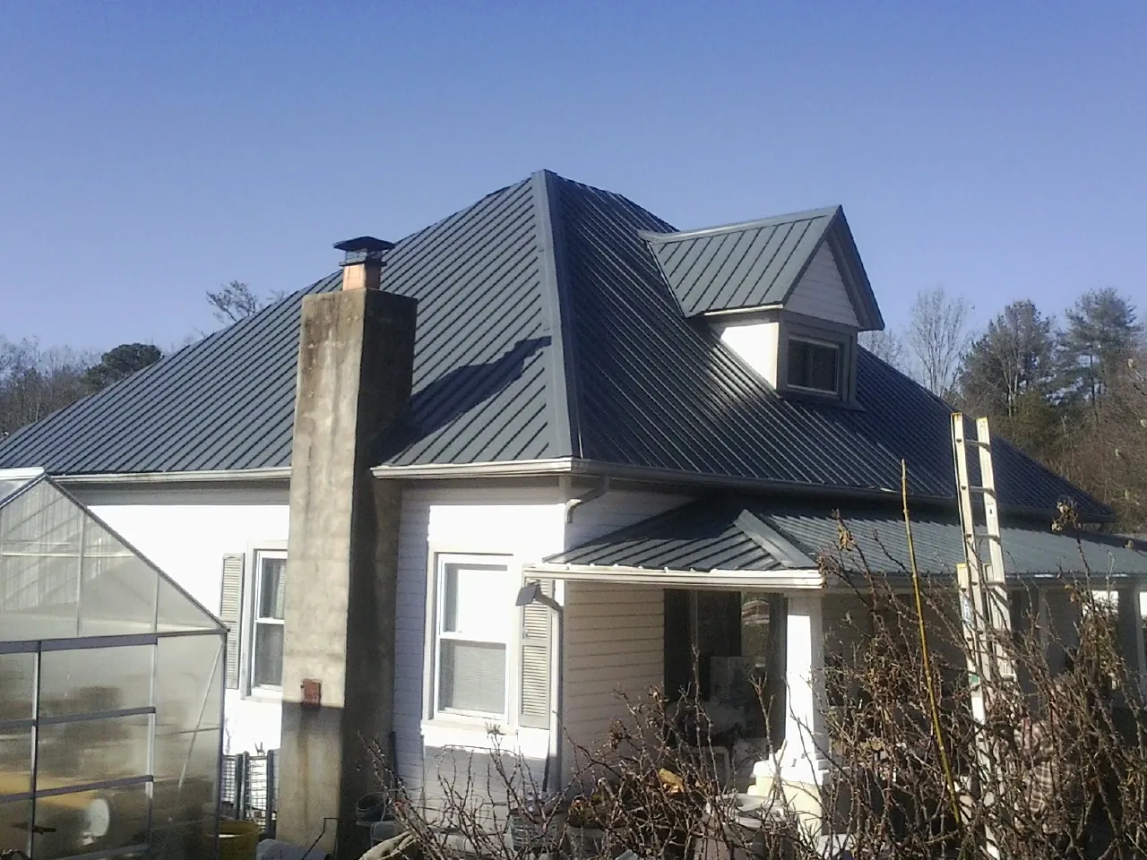 Dark blue standing seam metal roof on a white farmhouse with dormer — Slate & Tile Roof Repair by Roofing Brothers in Canon