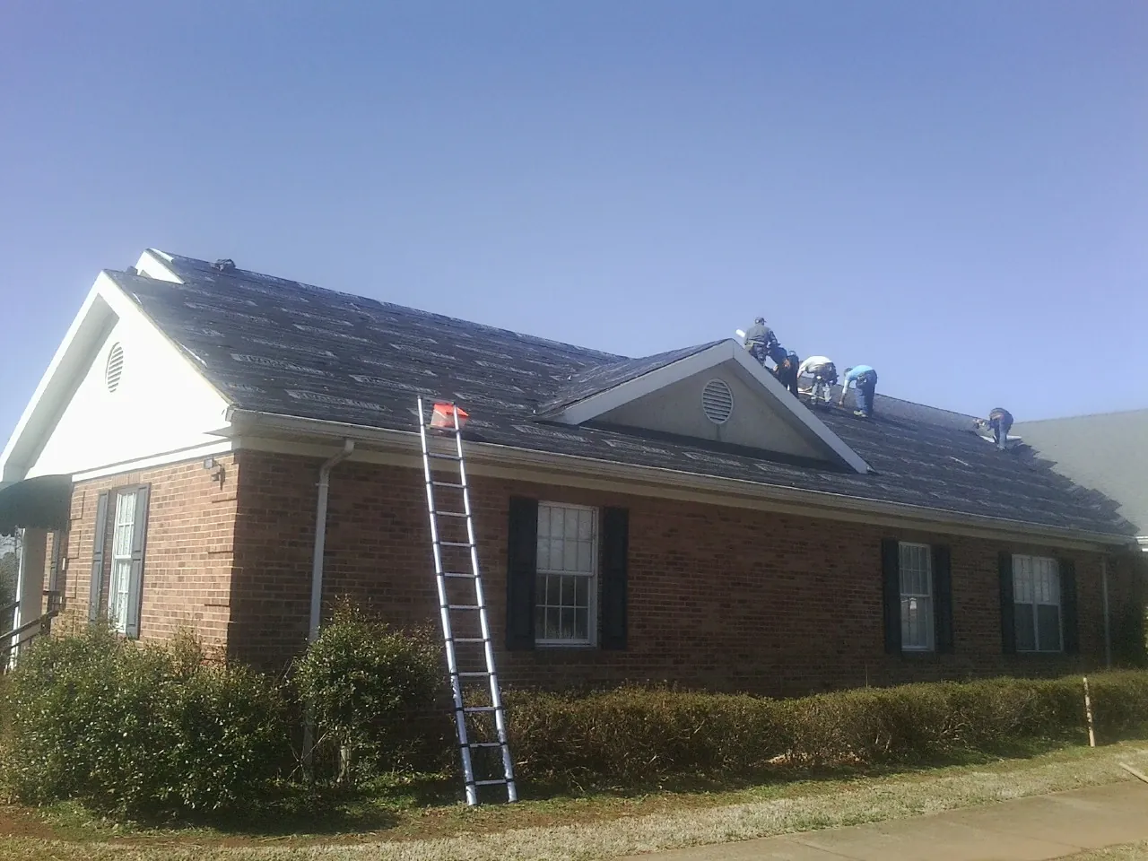 Crew tearing shingles off a brick ranch roof with a ladder set — Emergency Roof Repair work by our crew in Canon