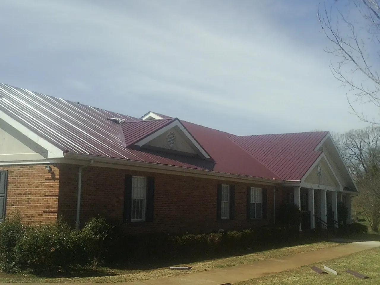 Red metal roof with gabled entries on a long brick building, from a Hail Damage Roof Repair job in Canon