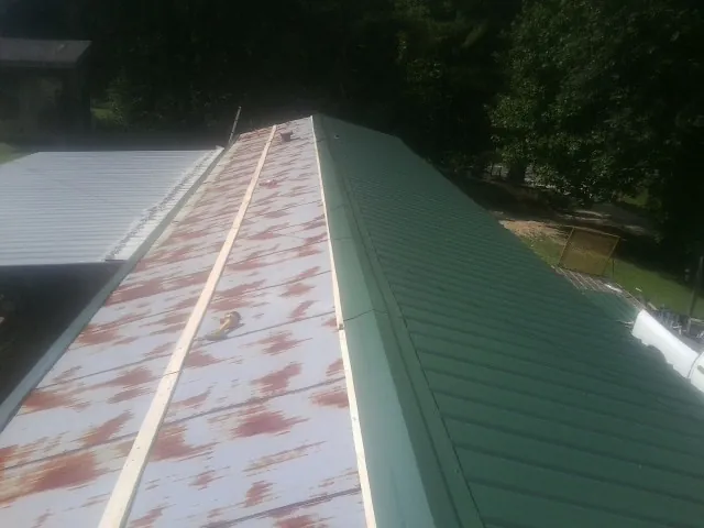 Old rusted panels beside newly installed green metal roofing — Wind Damage Roof Repair by Roofing Brothers in Canon