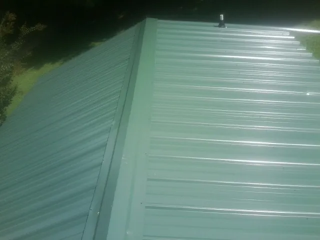 New green metal panels meeting at the ridge of a roof — Flat Roof Repair work by our crew in Canon