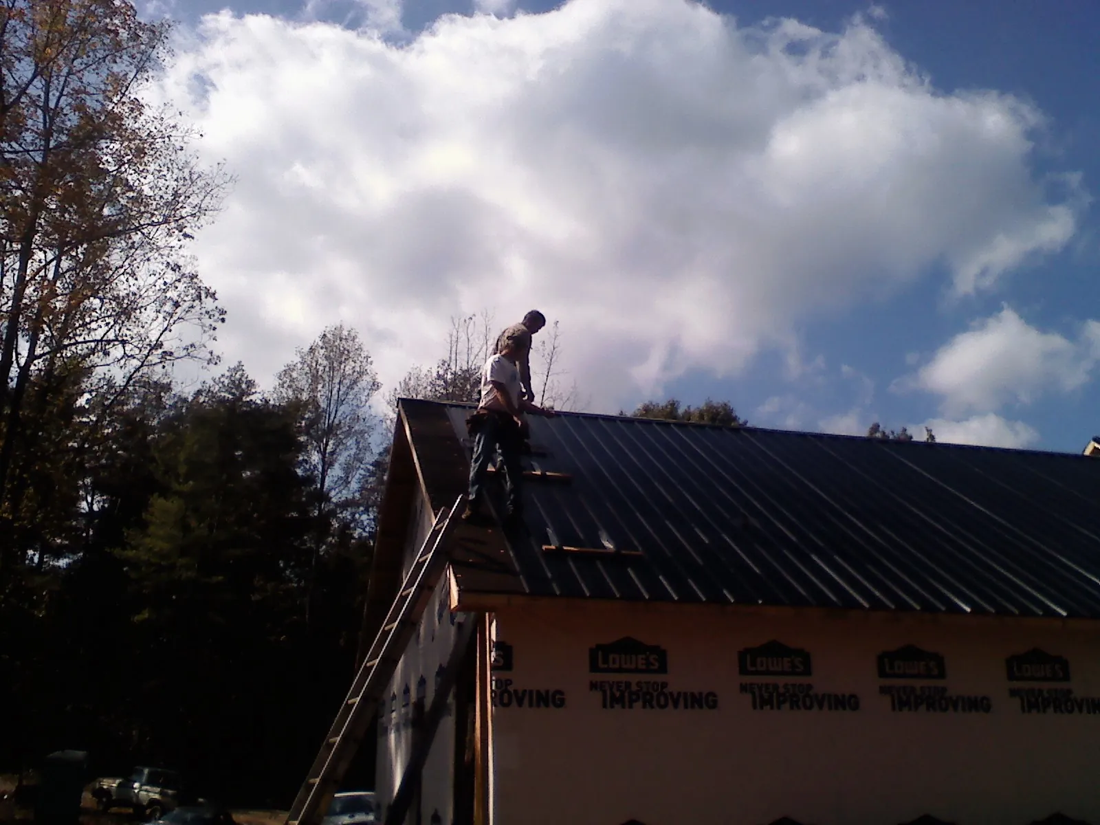 Roofer fastening dark metal panels high against a cloudy sky, from a Roof Inspection job in Canon