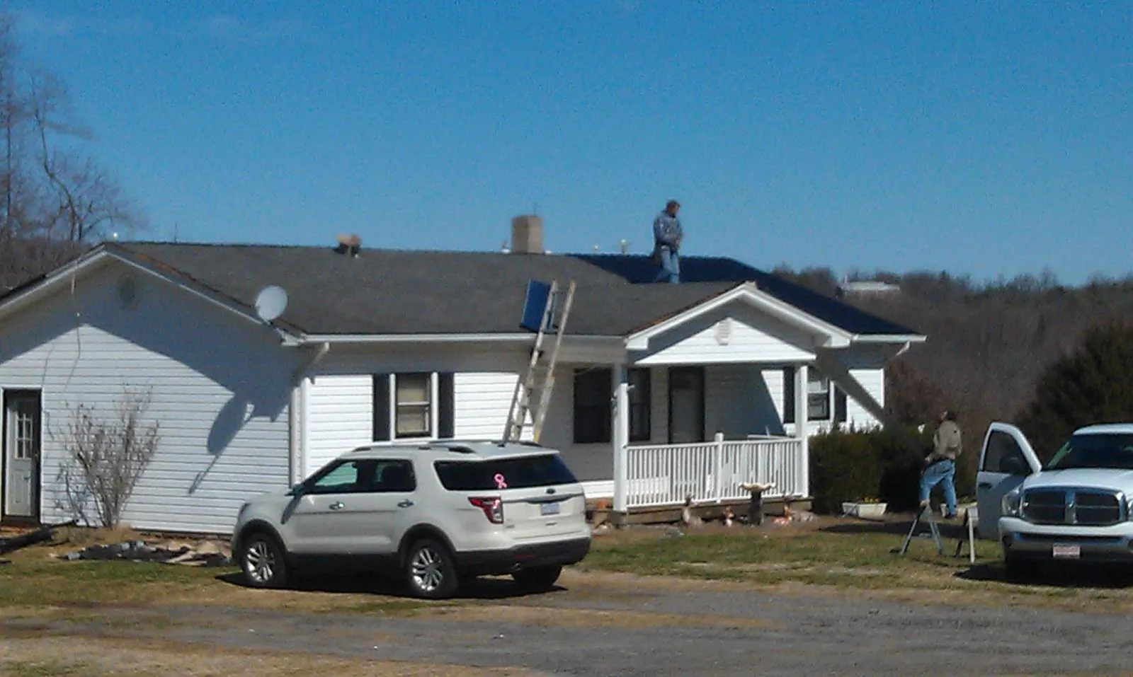 Roofers stripping shingles from a white ranch house roof in Canon