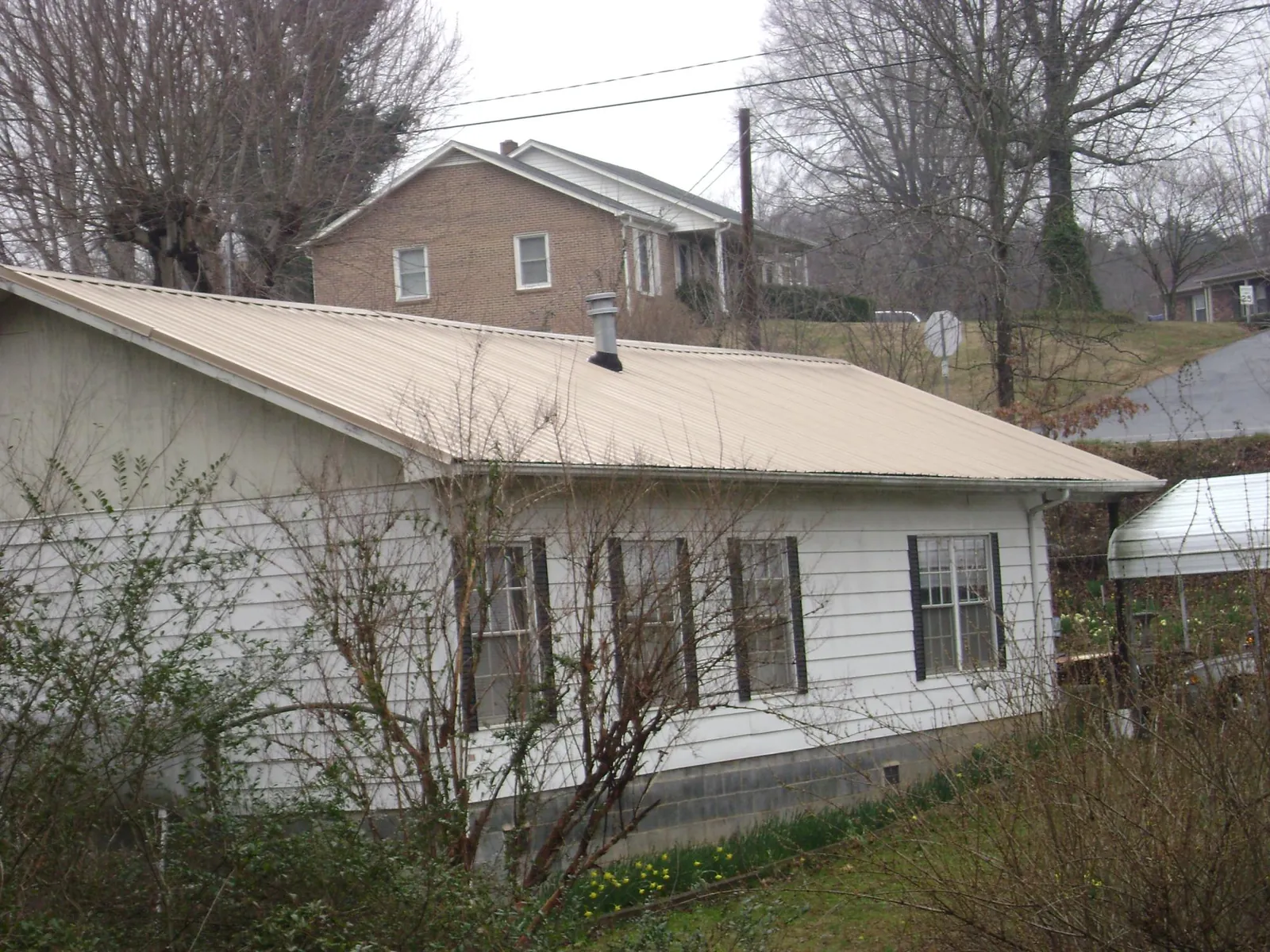Tan metal roof on a white sided house set into a hillside — Commercial Roofing by Roofing Brothers in Canon