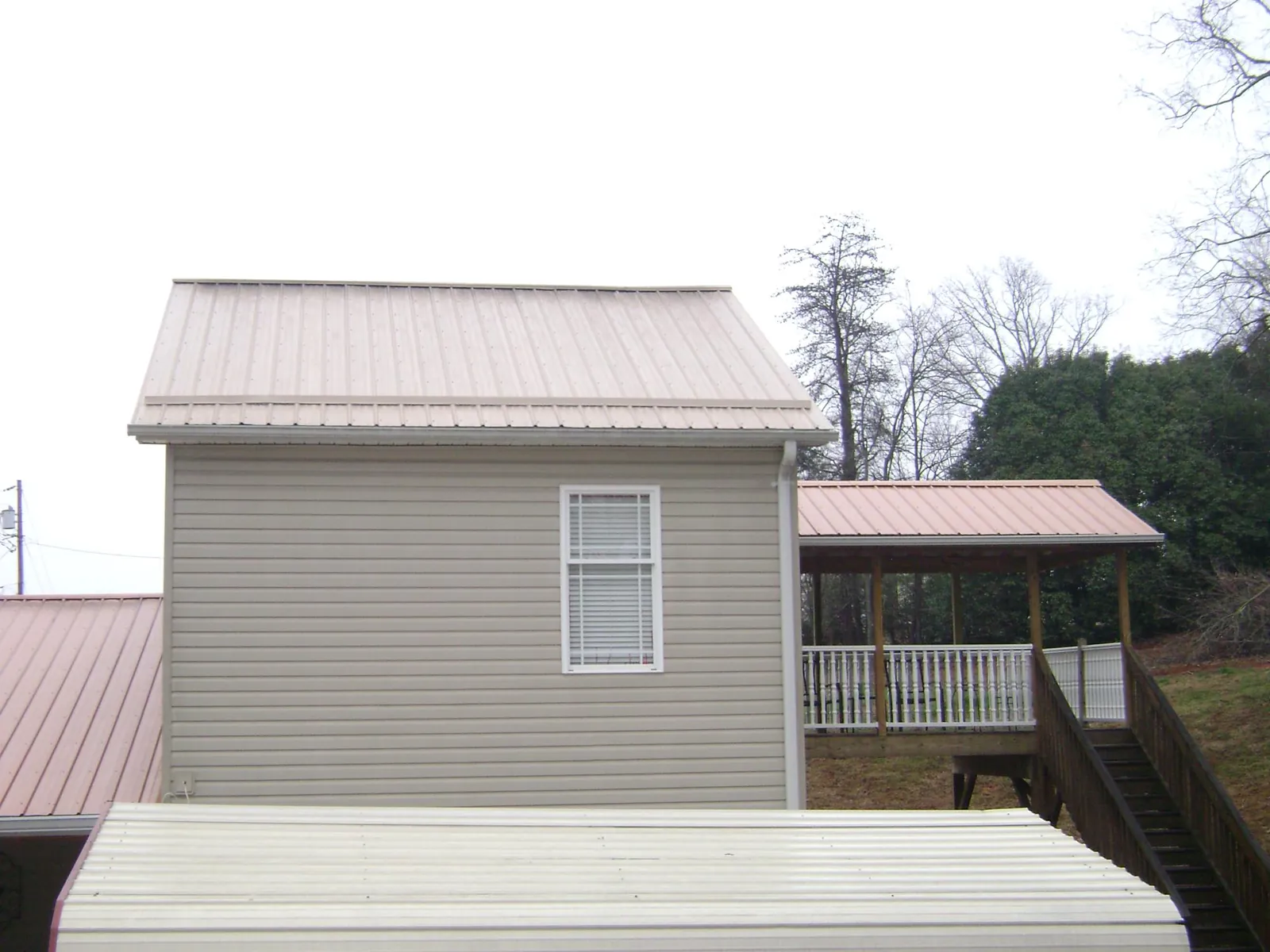Tan metal roofs on a two story addition and attached porch, from a Roof Replacement job in Canon